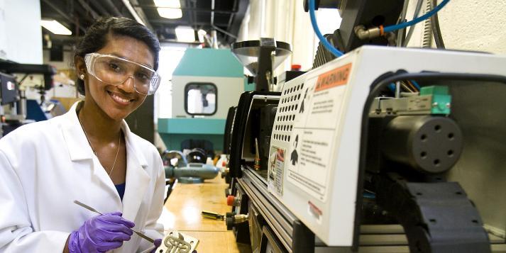 Student in white lab coat next to industrial machinery